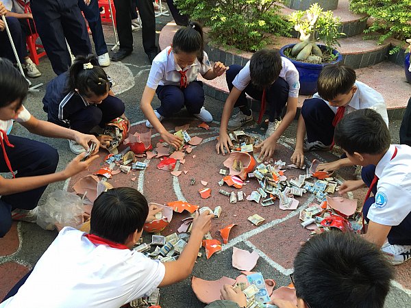 Các em học sinh đại diện cho lớp đang tiến hành đập heo đất tiết kiệm.